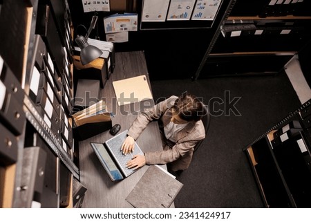 Top view of secretary typing administrative report on laptop computer, analyzing bureaucracy record in arhive room. Businesswoman working late at night at management system. Storage concept