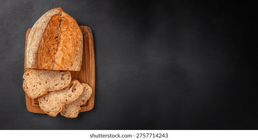 Top view of seeded bread loaf with sliced pieces on wooden board over black background with wide copy space for bakery design