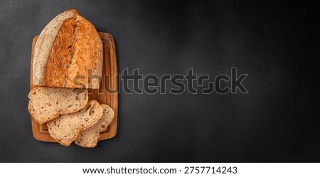 Top view of seeded bread loaf with sliced pieces on wooden board over black background with wide copy space for bakery design