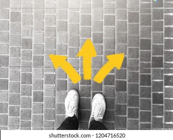 Top view of selfie feet on concrete floor background with yellow drawn left right toward direction arrows , decision making , Choices concept, where to go, directions, business solutions,uncertainty