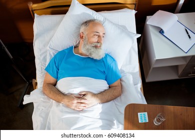 Top view of senior bearded man lying in hospital bed and lookig at distance - Shutterstock ID 609408134