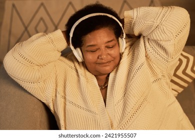 Top view of senior Black woman listening to music with eyes closed relaxing and wearing headphones lying down, copy space - Powered by Shutterstock