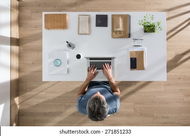 top view, senior executive sitting at  desk and working on his laptop, his table is perfectly tidy, the sun casts graphics shadows on the wood floor - Powered by Shutterstock