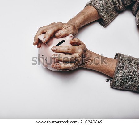 Top view of senior woman hands holding a piggy bank on grey surface. Elderly hands grabbing a small piggybank. Concept of secure investments.