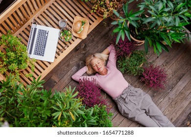 Top View Of Senior Woman With Laptop Lying Outdoors On Terrace, Resting.