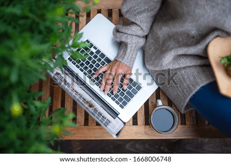 Top view of senior woman with laptop sitting outdoors on terrace, working.
