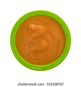 Top View Of A Serving Of Banana Carrot And Mango Baby Food In A Green Bowl Isolated On A White Background.