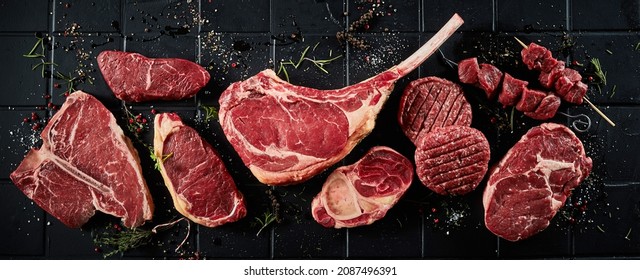Top view of set of various uncooked stakes including t bone tomahawk sirloin ribeye beef and cutlets with shashlik topped with spices and black surface - Shutterstock ID 2087496391