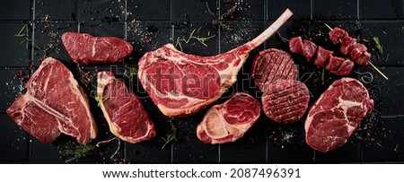 Top view of set of various uncooked stakes including t bone tomahawk sirloin ribeye beef and cutlets with shashlik topped with spices and black surface