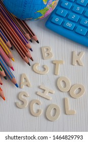 Top view of several diagonal colored pencils, world ball and blue calculator, with the words back to school unlinked, on white wooden background in vertical