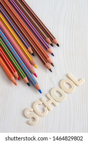 Top view of several diagonal colored pencils with the word school, on white wooden background in vertical