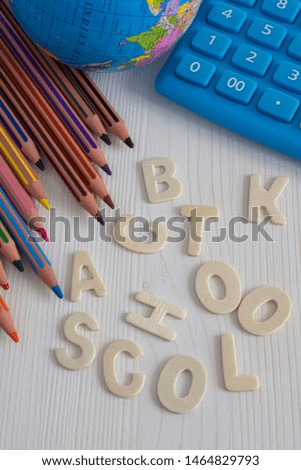 Top view of several diagonal colored pencils, world ball and blue calculator, with the words back to school unlinked, on white wooden background in vertical