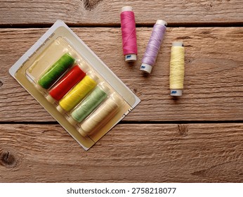 Top view of several spools of thread and a plastic package on a wooden table.