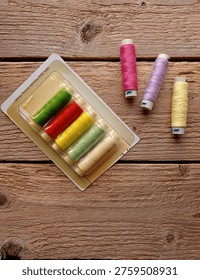 Top view of several spools of thread and a plastic package on a wooden table.