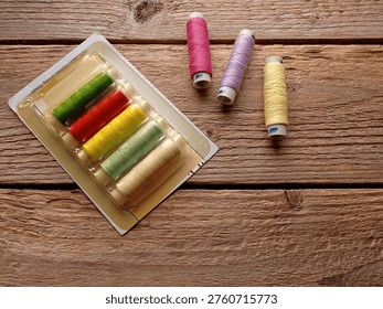 Top view of several spools of thread and a plastic package on a wooden table.
