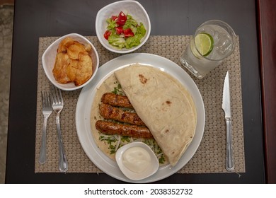 A Top View Of Shish Taouk, Bread, Sesame Paste , And Cutlery On A White Plate On A Gray Table