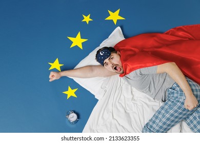 Top View Shocked Young Man 20s Wear Pajamas Jam Sleep Mask Red Superhero Suit Rest Relax Home Lie Make Fly Gesture Isolated On Dark Blue Sky Background. Night Bedtime Supernatural Abilities Concept