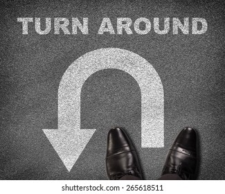 Top View Of Shoes Standing On Asphalt Road With U-turn Sign And Text Turn Around. Business Concept