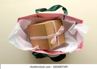 Top View Of Shopping Bag And Gift Box On It, White Tissue Wrapping Paper On The Bright Desk.Craft Gift Box With Pink Ribbon,bow In The Bag