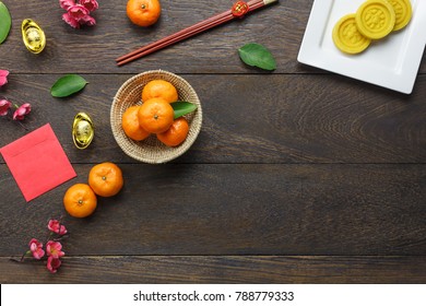 Top View Shot Of Arrangement Decoration Chinese New Year & Lunar Holiday Background Concept.Flat Lay Orange & Dessert Also Red Pocket Money On Modern Brown Wooden At Home Desk.Free Space For Mock Up.