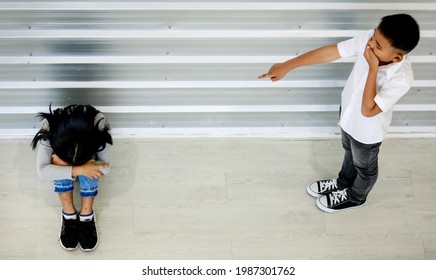 Top view shot of Asian young unruly rowdy crazy boy standing laughing blaming pointing bullying at small little upset sad girl sitting on floor cover face between knees crying alone in primary school.