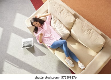 Top View Shot Of Beautiful Brunette Female Using Her Mobile Phone While Lying On Sofa At Home.