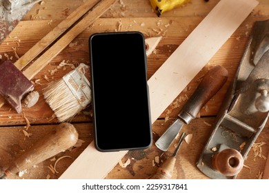 Top view shot of cell phone with empty display on table among the shavings and set of carpentry tools, copy space for advertisement or promotional text.