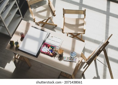 Top View Shot Of Drawing Painting Artist Hobby Workshop Studio Equipment On Wooden Table Including Canvas Easel Stand Watercolor Paintbrush Pencils Palette Tray Paper Under Strong Light From Outside.