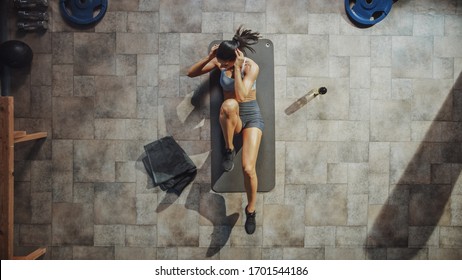 Top View Shot Of Professional Female Bodybuilder Doing Bicycle Crunches While Lying On The Yoga Mat In The Hardcore Gym. Muscular And Athletic Beautiful Woman Muscle, Power And Cardio Workout.