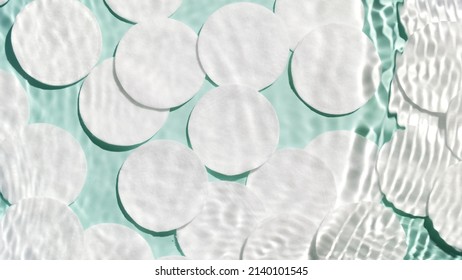 Top view shot of water ripples over cotton pads laying on pale green background | Background shot for face care product - Shutterstock ID 2140101545