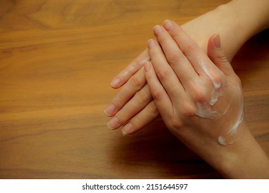 A Top View Shot Of A Woman Putting Hand Cream On Her Hand On A Wooden Table