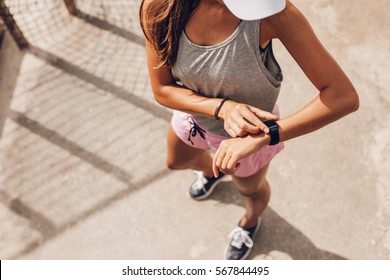 Top view shot of young woman checking fitness progress on her smart watch. Female runner using fitness app to monitor workout performance.