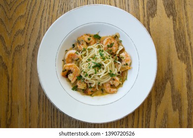 Top View Of Shrimp Scampi Linguine On A White Plate Against Wooden Background.