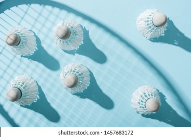 top view of shuttlecocks with feathers near shadow of badminton racket on blue 
