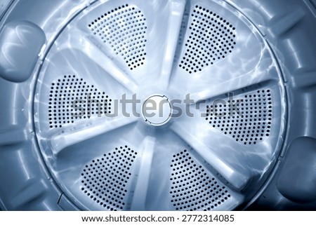Top view of a silver circular pulsator plate inside a washing machine with water drainage holes and bright light reflections