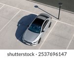 Top view of a silver sedan parked in an empty parking lot, casting a long shadow under clear sunlight. The minimalistic scene is captured from above, showcasing the car