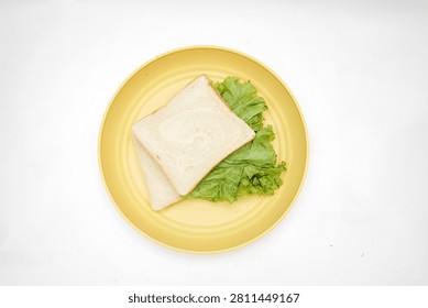 Top view of a simple white bread sandwich filled with green lettuce and served on a round yellow plate, isolated on a clean white background.