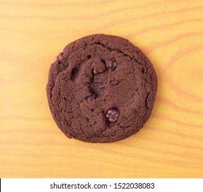 Top View Of A Single Double Chocolate Chip Cookie On A Yellow Wood Grain Background.