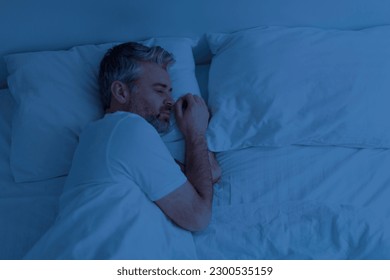 Top view of single handsome grey-haired middle aged man wearing pajamas peacefully sleeping alone in bed at night at home, empty pillow and free space next to him - Powered by Shutterstock