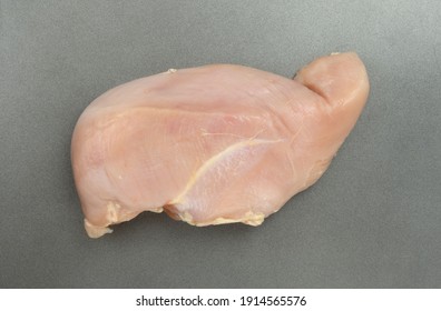 Top view of a single large raw chicken breast on a square defrosting metal.