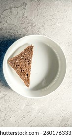 Top view of a single slice of triangle whole grain rye bread served on a white plate with copy space