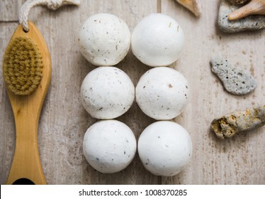 top view of six bath bombs with a wooden bath brush and sea shells on top of a tile background