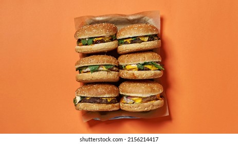 Top View Of Six Classic Delicious And Appetizing Fresh Burgers On Craft Recyclable Paper In Tray. Unhealthy Eating And Fast Food. High-calorie Sandwiches. Orange Background. Studio Shoot. Copy Space