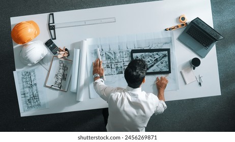 Top view of skilled architect looking at project plan at tablet. Aerial view of civil engineer planning while checking building blueprint at meeting room with safety helmet and laptop. Alimentation. - Powered by Shutterstock