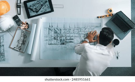 Top view of skilled engineer selecting material for house design while sitting at meeting table with tablet, laptop, safety helmet and equipment. Smart architect looking at project plan. Alimentation. - Powered by Shutterstock