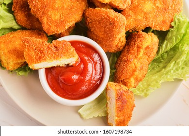 Top view sliced chicken nuggets in ketchup in a plate with a bunch of nuggets and lettuce.