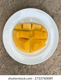 Top View Of Sliced Mango With A Grid Pattern On A White Plate, Placed On A Tile Surface.