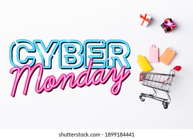 Top view of small gift boxes and shopping bags near toy cart and cyber monday lettering on white background