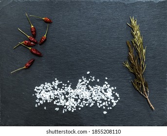Draufsicht von kleinen roten Paprika, Rosmarin und Salz auf einem schwarzen Schieferboden
