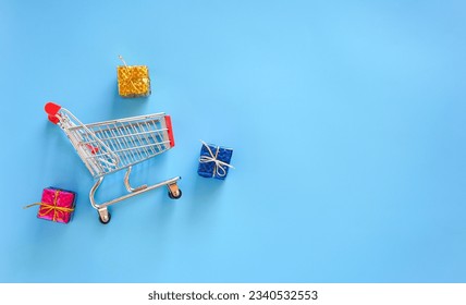 Top view of small shopping cart and gift box on blue background with copy space. - Powered by Shutterstock